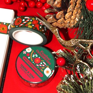 This Christmas washi tape features abstract holiday shapes of various styles of ornaments, garlands, tree decor, and mistletoes. This is a dark green washi tape, with white and red elements, and gold foiling details. Pictured is a roll and packaging.
