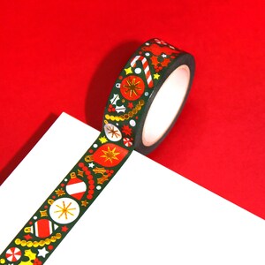 May include: A roll of green washi tape with a festive Christmas design. The tape features red and gold ornaments, candy canes, holly, and stars.