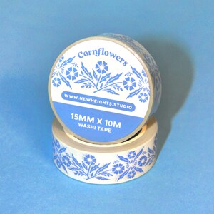 May include: Two rolls of washi tape with a blue floral design on a white background. The tape is labeled "Cornflowers" and "15mm x 10M Washi Tape". The website address www.newheights.studio is also visible.