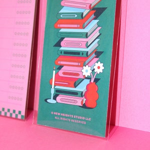 May include: A stack of colorful books with a candle and a vase of flowers on a green background. The text "&copy; NEW HEIGHTS STUDIO LLC ALL RIGHTS RESERVED" is at the bottom of the image.