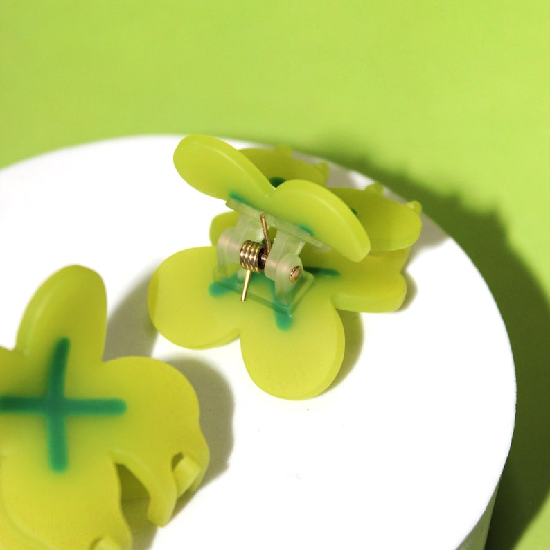 Pode incluir: Dois grampos de cabelo de pl&aacute;stico verde em forma de trevo de quatro folhas. Os grampos t&ecirc;m um mecanismo de mola e s&atilde;o projetados para segurar o cabelo no lugar.