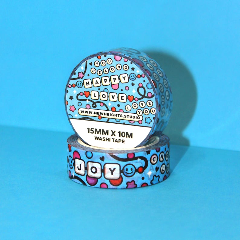 May include: Two rolls of blue washi tape with a colorful pattern of hearts, stars, and smiley faces. The tape features the words "You Belong Happy Love" and "Joy" in a blocky font. The tape is 15mm wide and 10m long.