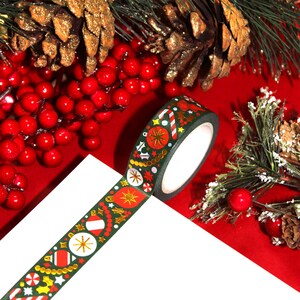 May include: Green washi tape with gold foil accents featuring a Christmas theme with ornaments, candy canes, and stars. The tape is rolled up and partially unrolled on a white surface.