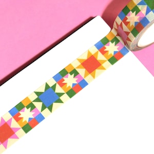 May include: Decorative washi tape roll with a colorful geometric pattern. The design features squares and star shapes in red, blue, green, yellow, and pink. The tape is on a white surface with a pink background.