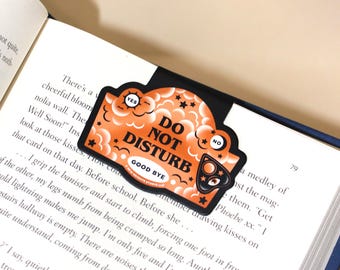 May include: Orange and black bookmark with the text "Do Not Disturb" and "Good Bye" in a cloud-like design with stars and a black cat eye.