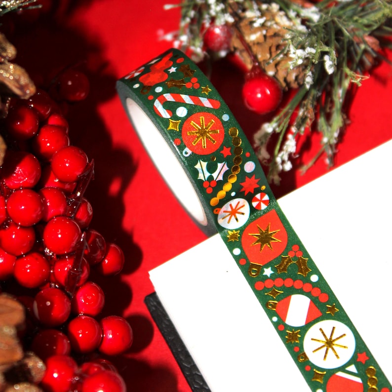May include: A roll of green washi tape with a Christmas theme. The tape features red and gold ornaments, candy canes, holly, and stars.