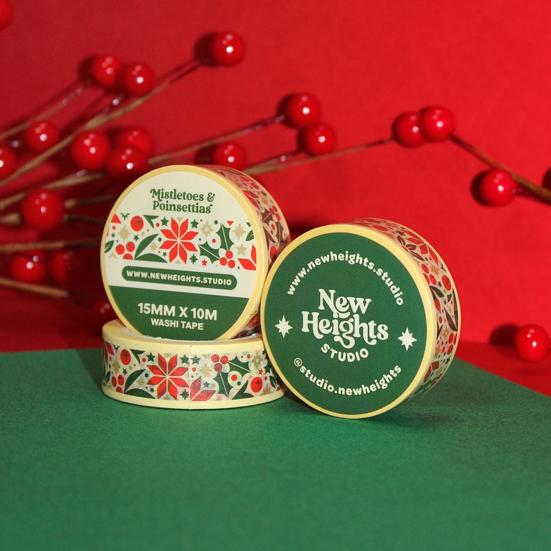 May include: Three rolls of washi tape with a Christmas theme. The tape features a green and gold background with red poinsettias and holly. The text on the tape reads "Mistletoes & Poinsettias", "www.newheights.studio", "15MM X 10M WASHI TAPE", "New Heights Studio", and "@studio.newheights".