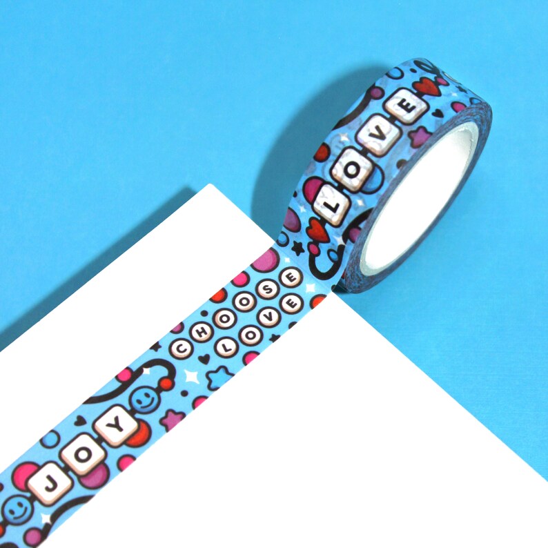 May include: A blue washi tape with a repeating pattern of hearts, stars, and smiley faces. The tape has the words "Choose Love" and "Joy" printed on it.