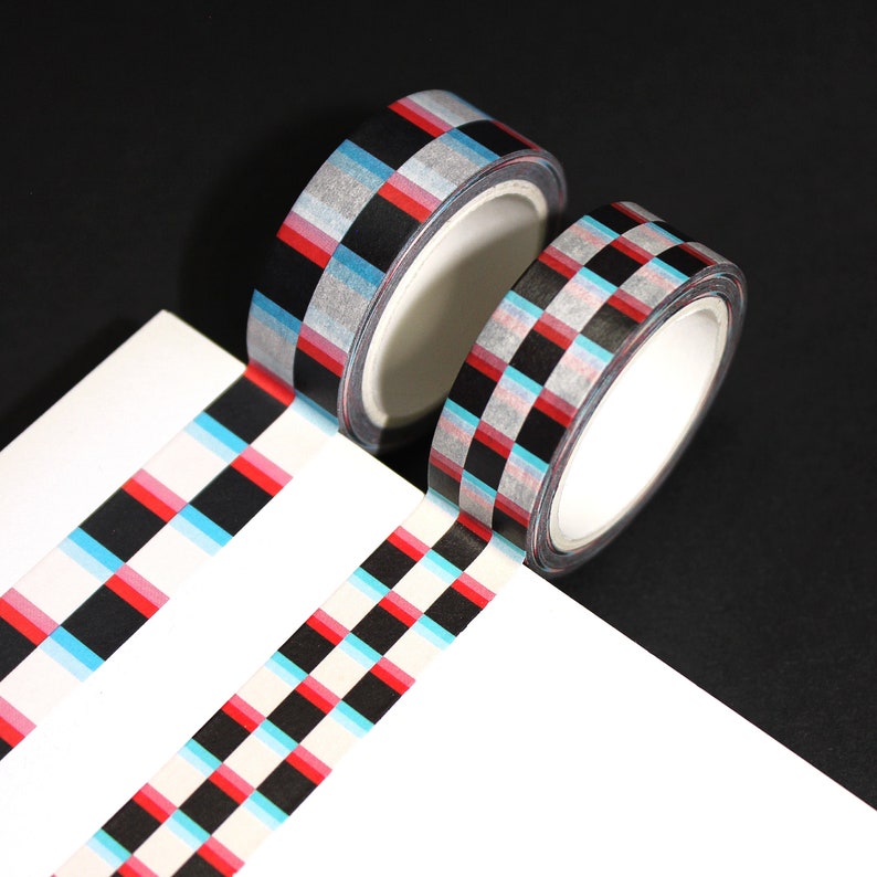 May include: Two rolls of washi tape with a checkered pattern in black, red, blue, and white. The tape is on a white surface.