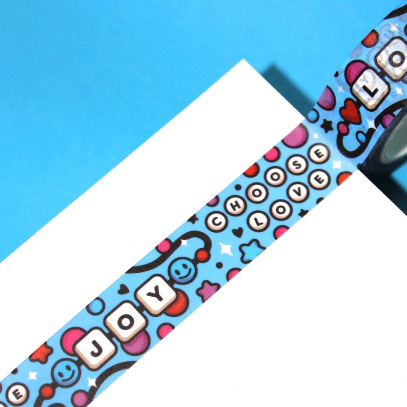 May include: A blue and white washi tape with a repeating pattern of colorful circles, stars, hearts, and smiley faces. The tape features the words "Choose Love" and "Joy" in white letters.