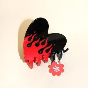 This is a glossy, heart-shaped accessory in black with vibrant red flames and adorned with red rhinestones that sparkle like hot embers.