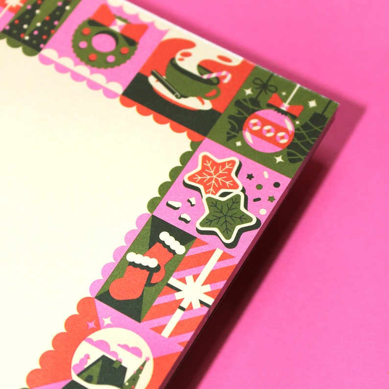 Peut inclure: Un bloc-notes d&eacute;coratif avec un bord festonn&eacute; rose et une bordure &agrave; th&egrave;me de No&euml;l r&eacute;p&eacute;titive. La bordure pr&eacute;sente des illustrations festives d'ornements, de biscuits et de cadeaux dans des tons de vert, de rouge et de rose. Le bloc-notes a un int&eacute;rieur blanc.