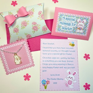 May include: A pink and white gift box with a pink bow and a white bunny charm necklace. The box has a floral pattern and the necklace has a pink heart on the bunny. The card says "A special message for Scarlett" and "Dear Scarlett, I heard that you have been very well behaved recently, so I thought I would leave you a special gift for Easter. Chocolate eggs are yummy, but here is something you can keep forever. I hope you enjoy wearing it. Have a very happy Easter and see you next year. Love from The Easter Bunny XXX"