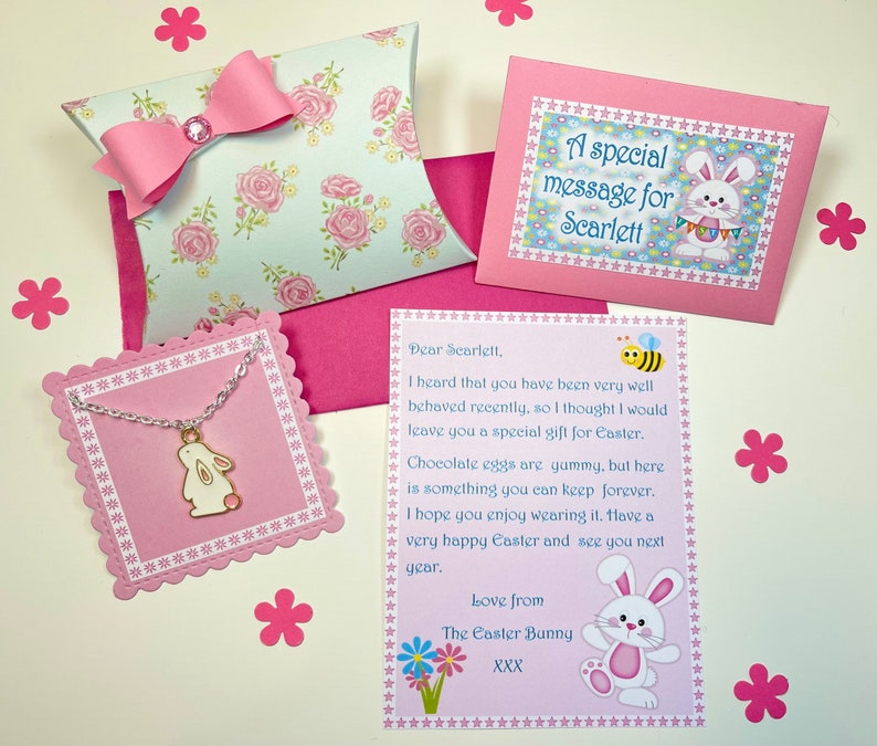 May include: A pink and white gift box with a pink bow and a white bunny charm necklace. The box has a floral pattern and the necklace has a pink heart on the bunny. The card says "A special message for Scarlett" and "Dear Scarlett, I heard that you have been very well behaved recently, so I thought I would leave you a special gift for Easter. Chocolate eggs are yummy, but here is something you can keep forever. I hope you enjoy wearing it. Have a very happy Easter and see you next year. Love from The Easter Bunny XXX"