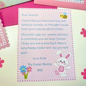 May include: A pink and blue card with a white bunny and a bee illustration. The card has a message for Scarlett, wishing her a happy Easter. The text reads: "Dear Scarlett, I heard that you have been very well behaved recently, so I thought I would leave you a special gift for Easter. Chocolate eggs are yummy, but here is something you can keep forever. I hope you enjoy wearing it. Have a very happy Easter and see you next year. Love from The Easter Bunny XXX"