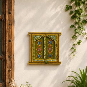 May include: A rectangular wall-mounted wooden window frame featuring two hinged doors painted in olive green. The doors are decorated with hand-painted floral patterns in blue, pink, and yellow, accented by white scrollwork and a mustard yellow border.