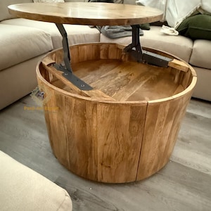 May include: A wooden round coffee table with a lift-top mechanism. The table has a natural wood finish and a circular base. The top lifts up to reveal storage space inside.