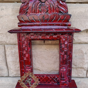 Puede incluir: Un marco de fotos de madera roja con tallas intrincadas. El marco tiene una parte superior decorativa con un diseño tallado. El marco mide aproximadamente 30 cm de alto y 20 cm de ancho.