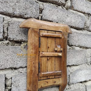 Puede incluir: Una pequeña puerta de madera con pomo de latón, montada en una pared de ladrillo. La puerta está cerrada y tiene un aspecto rústico y antiguo.