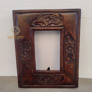 Pode incluir: Uma moldura de madeira marrom escura com intrincados desenhos florais esculpidos. A moldura tem uma abertura retangular para uma foto ou uma obra de arte.