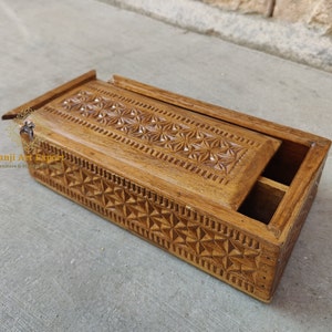 May include: A wooden box with a hinged lid, intricately carved with a geometric pattern. The box is made of light brown wood and has a natural finish. The lid is slightly ajar, revealing the interior of the box.