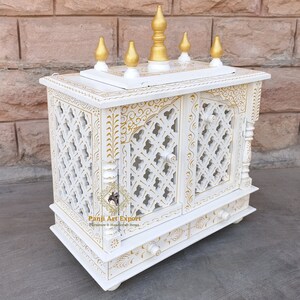 Puede incluir: Templo de madera blanco con detalles dorados y tallas intrincadas. El templo tiene dos puertas y un caj&oacute;n. Est&aacute; decorado con un dise&ntilde;o tradicional indio.