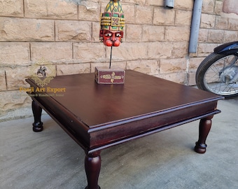 May include: A dark brown wooden coffee table with four turned legs. The table has a square top and a decorative border around the edge. A small wooden box with a painted design sits on the table.