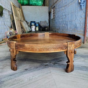 May include: A round wooden coffee table with intricate carvings around the edge of the tabletop and on the legs. The table has a dark brown wood finish.