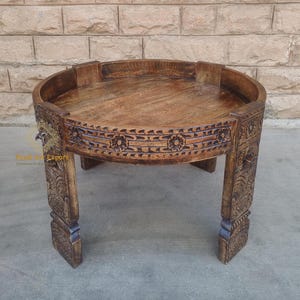 May include: A round wooden coffee table with intricate carvings on the legs and rim. The table has a dark brown finish and a raised edge around the top.