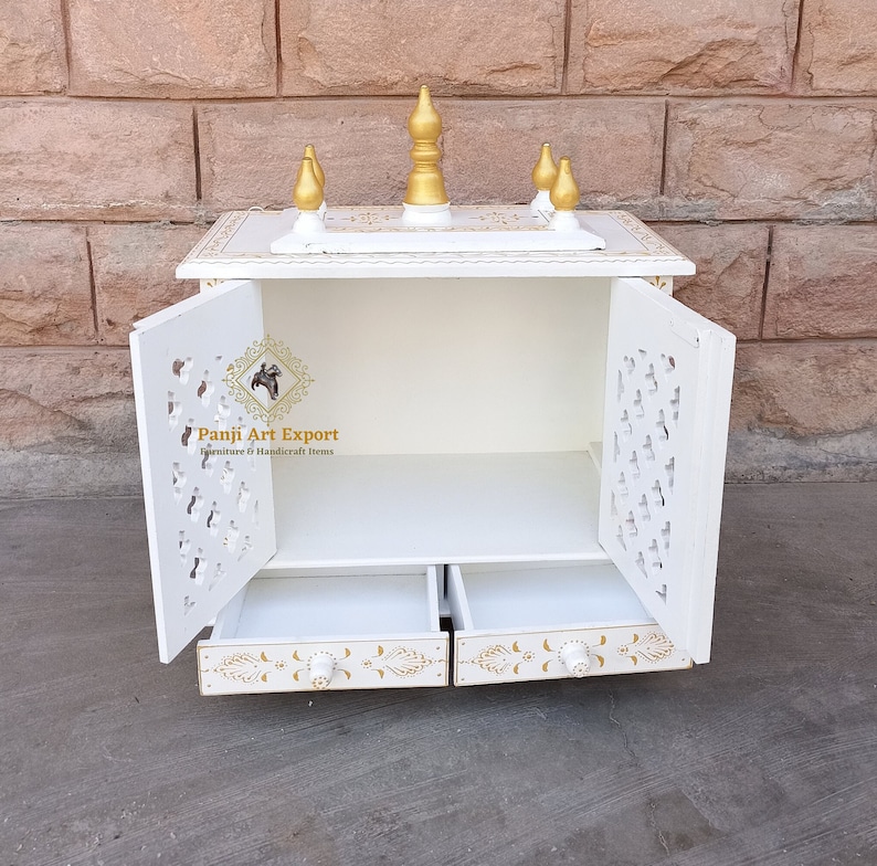 Puede incluir: Templo de madera blanco con dos puertas y dos cajones. Las puertas tienen recortes intrincados y los cajones tienen detalles dorados. El templo tiene un peque&ntilde;o techo con detalles dorados.