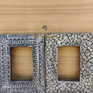 Puede incluir: Dos marcos de fotos de madera ornamentados con intrincados tallados. Los marcos son ambos negros y tienen un acabado desgastado. Los tallados son de estilo floral.
