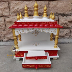 Può includere: Un tempio in legno bianco con una base rossa e dettagli dorati. Il tempio ha un piccolo cassetto e cinque decorazioni decorative in cima. Il tempio è dipinto con disegni intricati.