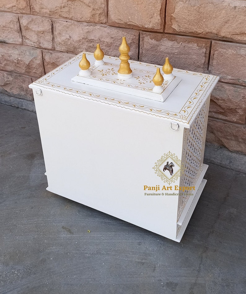 Puede incluir: Templo de madera blanco con detalles dorados y tallas decorativas. La parte superior del templo tiene cinco remates dorados. El templo est&aacute; sobre una superficie blanca. "Panji Art Export" est&aacute; impreso en el lateral del templo.