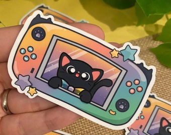 May include: A sticker of a black cat peeking out of a colorful video game console. The console is decorated with stars and has a rainbow-colored screen.