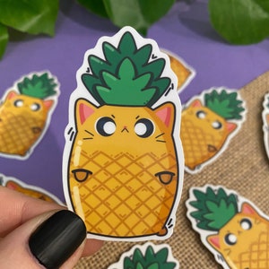 May include: A yellow pineapple with a green leafy top and a cat face. The pineapple has a cute, cartoon-like expression with large eyes and a small mouth.