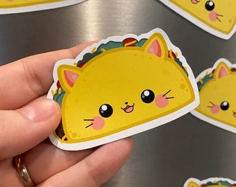 Può includere: Sei magneti a forma di taco di gatto giallo e bianco con facce sorridenti. I magneti sono su una superficie argentata.