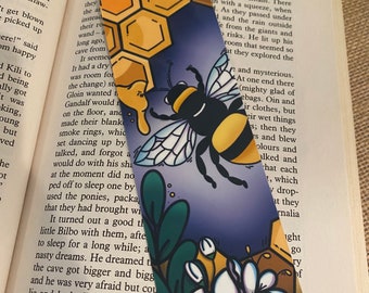 May include: A bookmark featuring a bee with yellow and black stripes, a honeycomb pattern, and white flowers on a purple background. The text "Over Hill and Under Hill" is printed at the top of the bookmark.