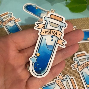 May include: A blue and white sticker of a glass test tube with a cork stopper. The test tube is filled with a blue liquid and has a white label that says "MANA". There are three small white stars and two small blue circles on the test tube.