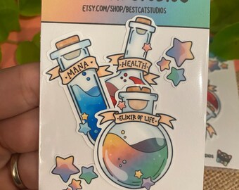 May include: A set of three colorful potion bottle stickers with star accents. The bottles are labeled "Mana", "Health", and "Elixir of Life". The stickers are from Best Cat Studios, with a website and social media hashtag.