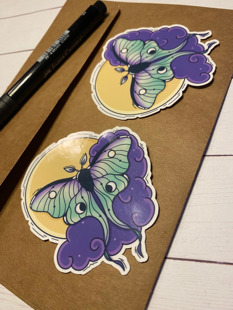 May include: Two stickers featuring a green and purple moth with large eyes on a yellow moon and purple clouds.