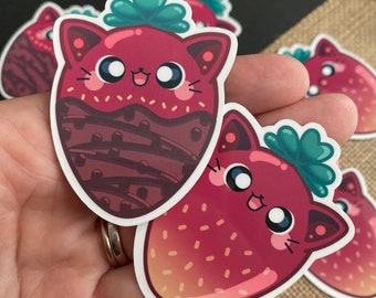 May include: Two cute cartoon strawberry stickers with cat faces. One strawberry is covered in chocolate with sprinkles and the other is a red strawberry with white seeds.