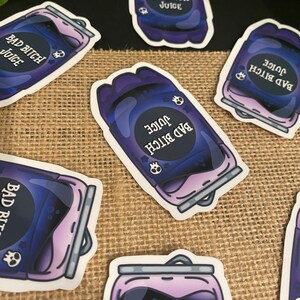 May include: A set of six stickers featuring a purple and black can with the text "Bad Bitch Juice" and a skull graphic. The stickers are on a burlap background.
