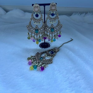 May include: A pair of silver earrings with pink, blue, green, and yellow beads hanging from them. The earrings are on a stand and there is a matching necklace with the same beads.
