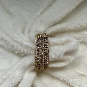 May include: A set of gold bangles with alternating rows of small beads and clear rhinestones.