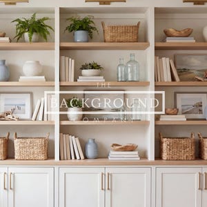 May include: A white, built-in bookcase with light wood shelves. The shelves are filled with books, decorative vases, framed art, woven baskets, and potted plants. The text "THE BACKGROUND COMPANY" is visible on the center shelves.