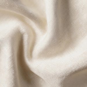 Puede incluir: Una pieza de tela color blanco roto con una textura tejida visible y un aspecto natural sin blanquear. El material est&aacute; drapeado en pliegues suaves y fluidos que crean sombras y reflejos sutiles en la superficie del tejido.