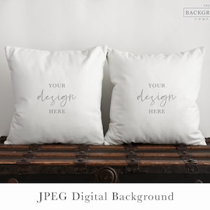 Könnte beinhalten: Zwei weiße Kissen mit dem Text "YOUR design HERE" auf jedem Kissen, die auf einer Holzkiste liegen. Der Hintergrund ist eine weiße Wand mit dem Text "THE BACKGROUND COMPANY" in der oberen rechten Ecke.