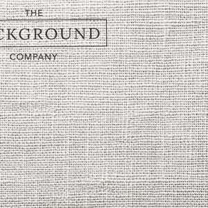 May include: A light gray, textured fabric surface with a visible woven pattern. In the upper left corner, there is a black rectangular border containing the text THE BACKGROUND COMPANY in a clean, sans-serif font, with the word COMPANY below it.