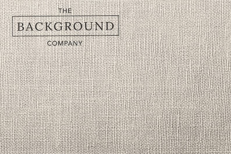 May include: A light beige fabric with a visible woven texture. In the upper left corner, a black rectangular border encloses the text THE BACKGROUND COMPANY, with the word BACKGROUND inside the box and THE and COMPANY placed above and below.