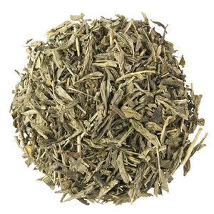 May include: Loose green tea leaves, a popular type of tea, are piled in a heap on a white background.